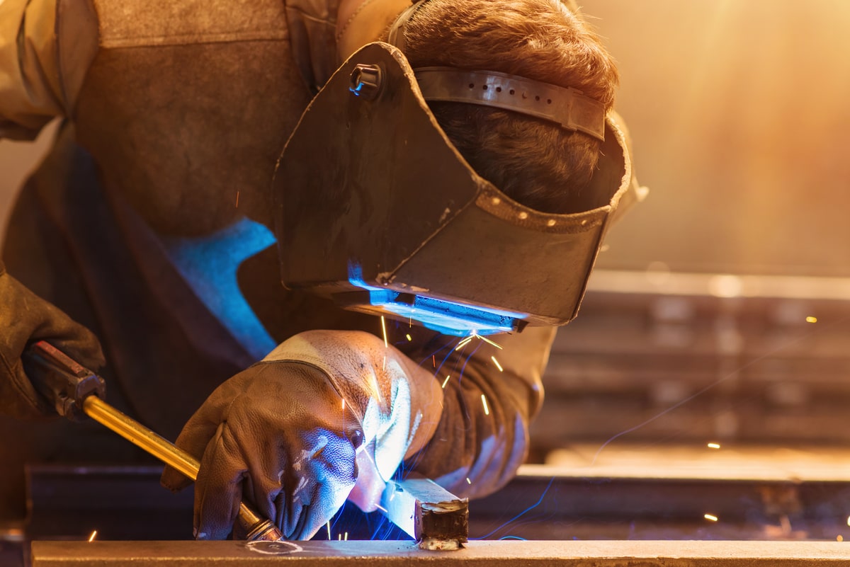 Man with flame-resistant clothes and protective mask welding in a factory.