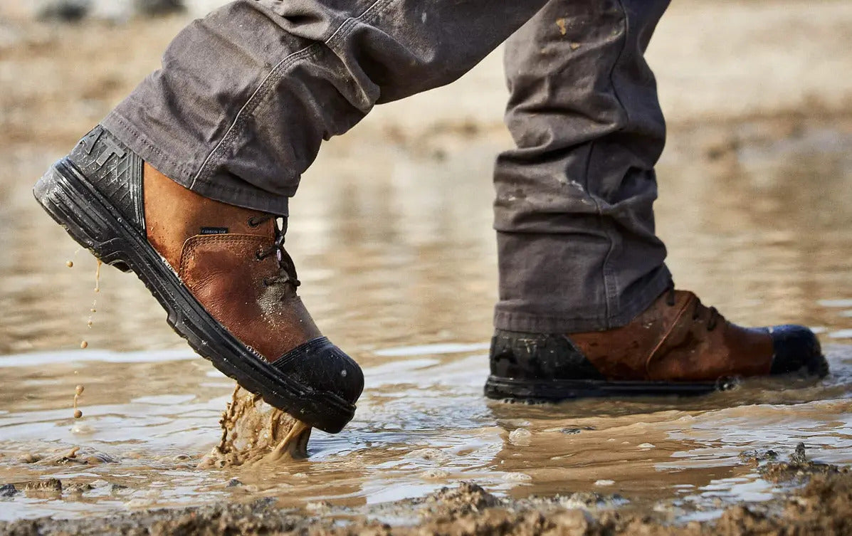 Worker wearing brown waterproof puncture-resistant boots walking through muddy construction site.