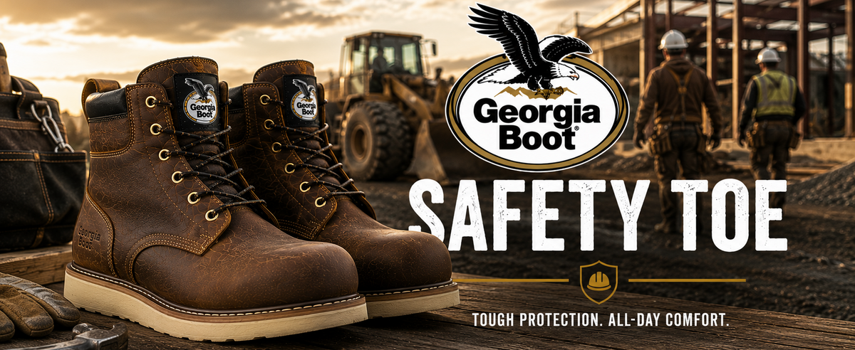 A pair of brown leather safety boots with steel-toe protection, displayed on a wooden surface in a construction site setting at sunset. The background shows construction workers and machinery, with the Georgia Boot logo and 'SAFETY TOE' text prominently displayed.