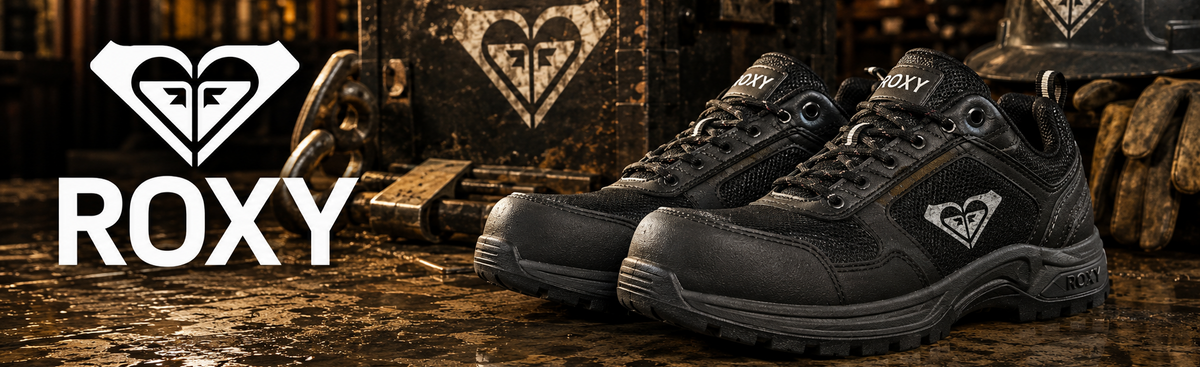 A pair of black Roxy work boots displayed on a wet, reflective industrial floor, with a branded helmet and a metal storage box in the background.