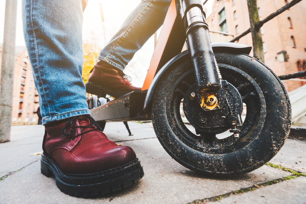 Close up of Electric scooter and women steel toe boots on pavement.