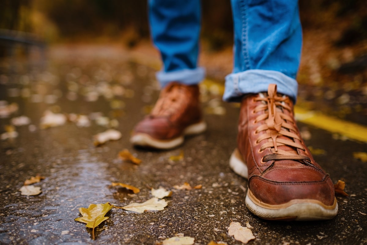 Feet of a Woman Walking Along Asphalt Road in Autumn.