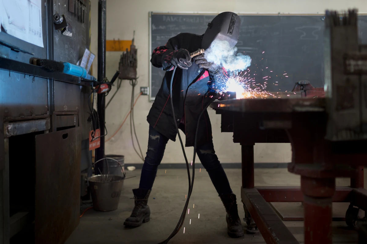 female metal worker in durable work boots welding at classroom