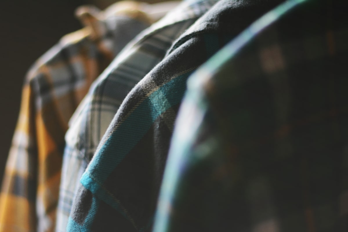 Flannel plaid shirts hanging in window light.