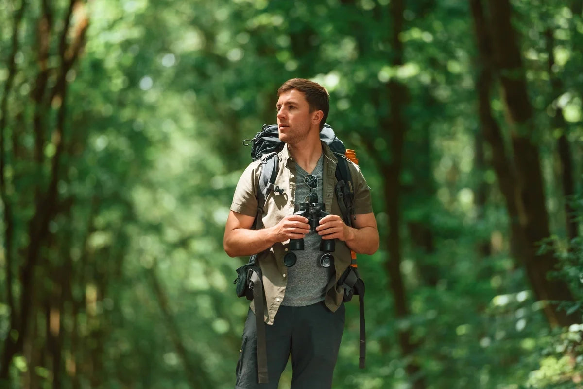 a mountaineer is standing in the forest and holding binoculars