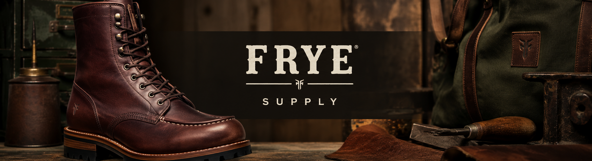 A brown leather lace-up work boot displayed on a rustic wooden surface with a dark central banner reading 'FRYE SUPPLY'. The scene includes leather tools, a green bag, and warm wood tones in the background.