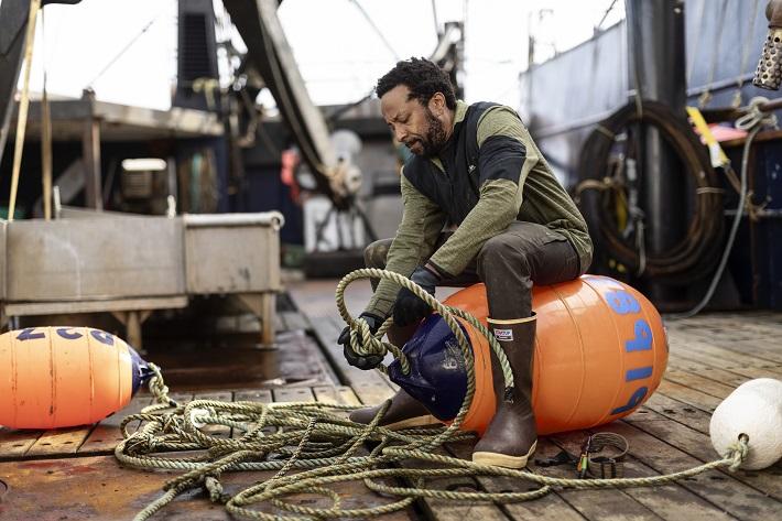a man in rubber boots is tying a buoy on a ship